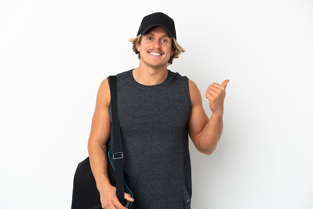 Young sport man with sport bag isolated on white wall pointing to the side to present a product