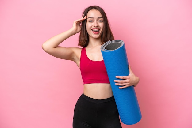 Young sport Ukrainian woman going to yoga classes while holding a mat isolated on pink background with surprise expression