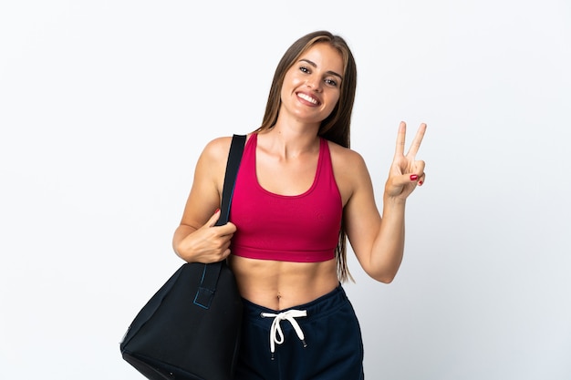 Young sport Uruguayan woman with sport bag isolated on white background smiling and showing victory sign