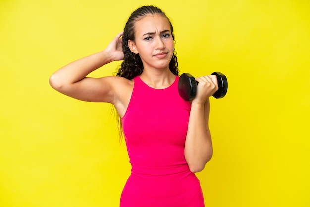 Young sport woman making weightlifting isolated on yellow background having doubts