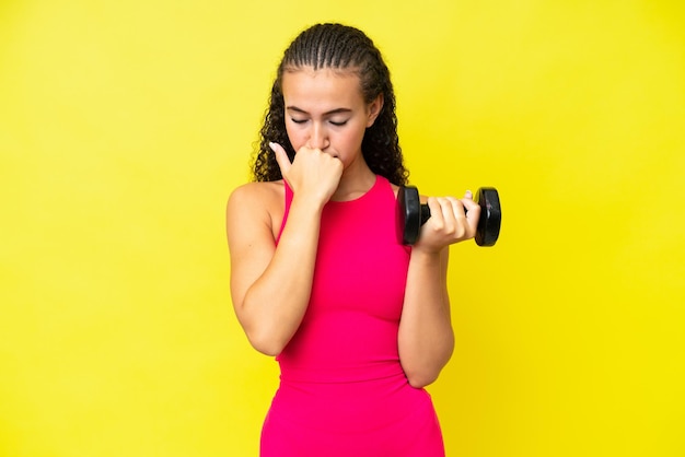 Young sport woman making weightlifting isolated on yellow background having doubts