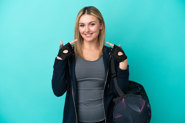 Young sport woman with sport bag isolated on blue background giving a thumbs up gesture