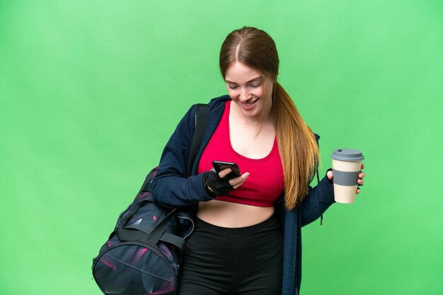 Young sport woman with sport bag over isolated chroma key background holding coffee to take away and a mobile