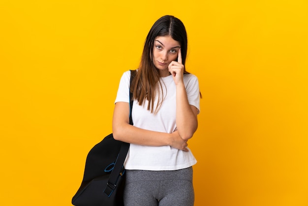 Young sport woman with sport bag isolated on yellow wall thinking an idea