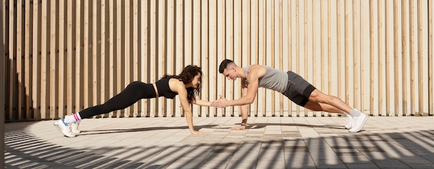 Young sportive couple in plank pose exercising together on sport street playground