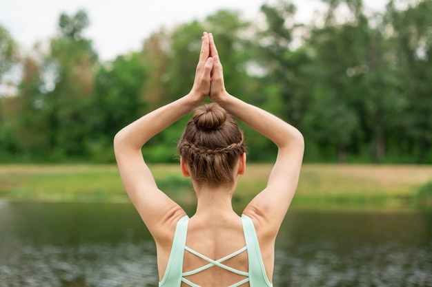 A young sports girl practices yoga on a green lawn by the river, yoga assans posture. Meditation and unity with nature