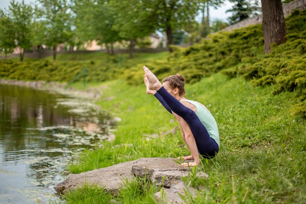 Photo young sports girl practices yoga on a green lawn by the river, yoga assans posture. meditation and unity with nature