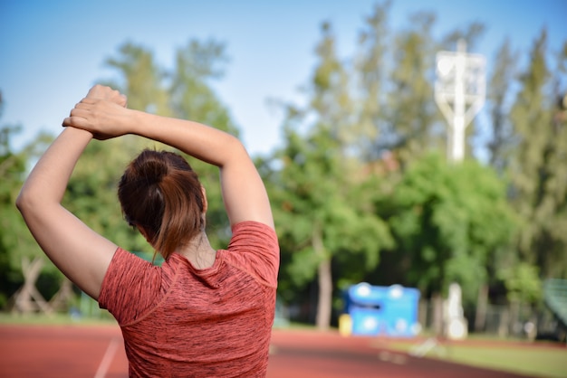 Young sports woman stretching her arms on stadium track before running.