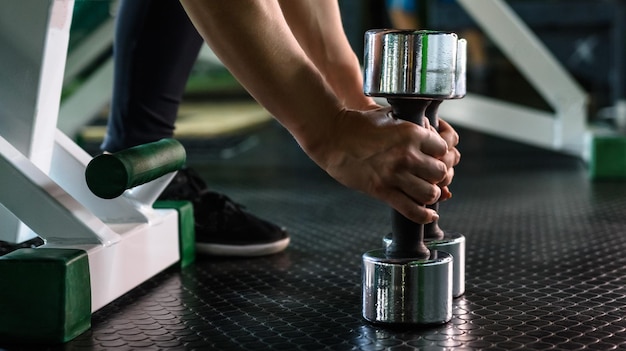 Young sports woman with dumbbells sitting on bench in the gym Fitness