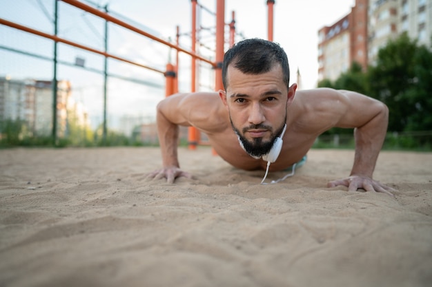 Young sportsman doing push ups and listening to music with headphones. Sport, fitness, street workout concept