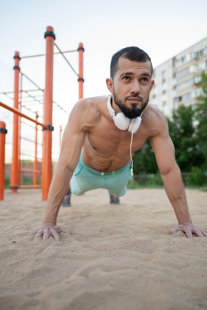 Young sportsman doing push ups and listening to music with headphones. Sport, fitness, street workout concept