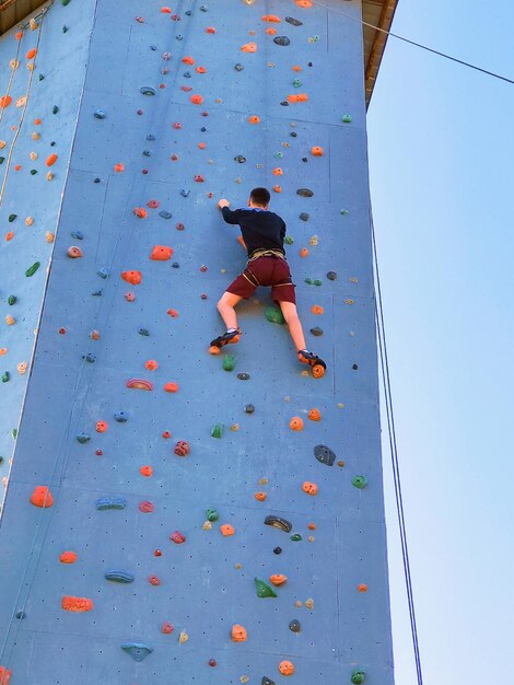 A young sportsman is climbing up the training wall for climbing View from below