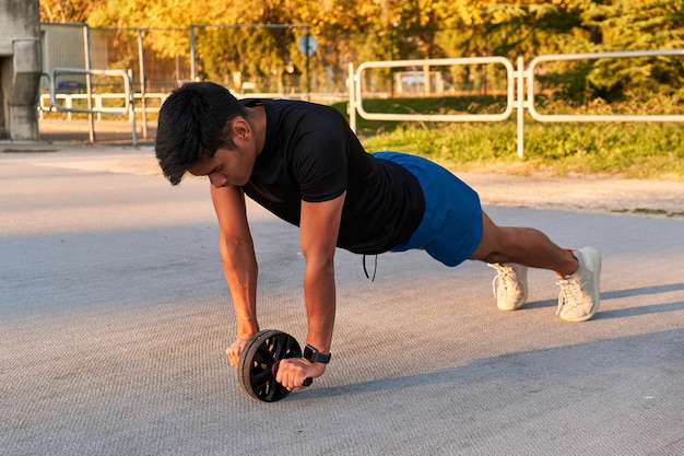 Young sportsman training with an abdominal roller wearing an smartwatch