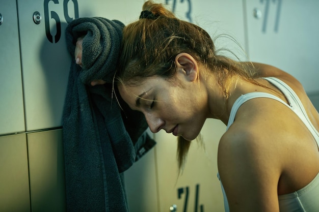 Young sportswoman feeling tired after working out and taking a break in gym's changing room