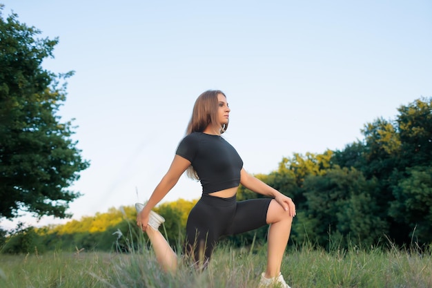 Young sportswoman in the park performs exercises for stretching the ligaments of the foot on the knee