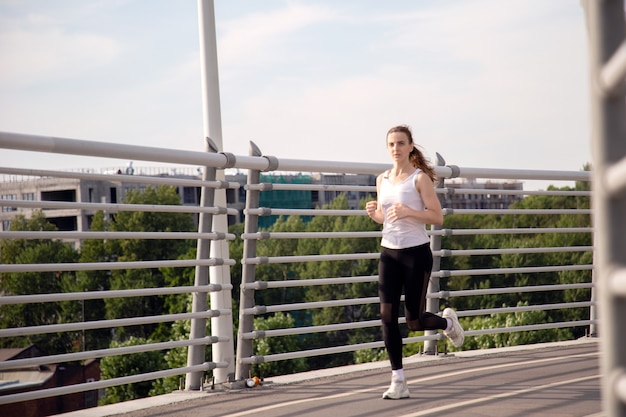 Young sportswoman running across the bridge