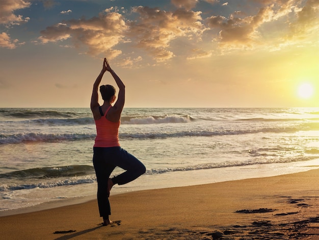 Young sporty fit woman doing yoga tree asana on beach