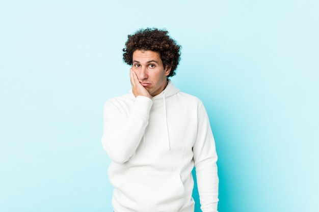 Young sporty man against a blue wall who is bored, fatigued and need a relax day.