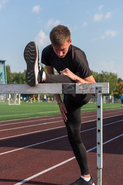 Young sporty man athlete runner in sportswear stretching before running hurdles on stadium