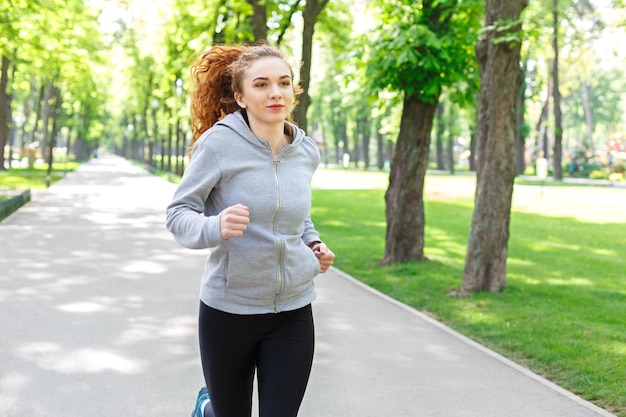 Young sporty woman jogging in green park during morning workout, copy space