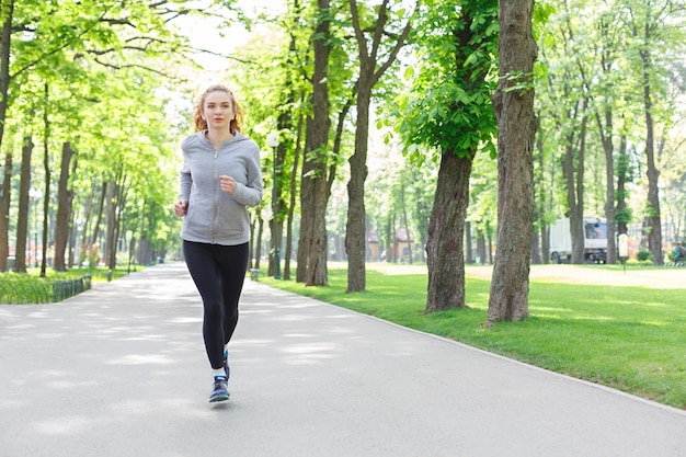 Young sporty woman jogging in green park during morning workout, copy space