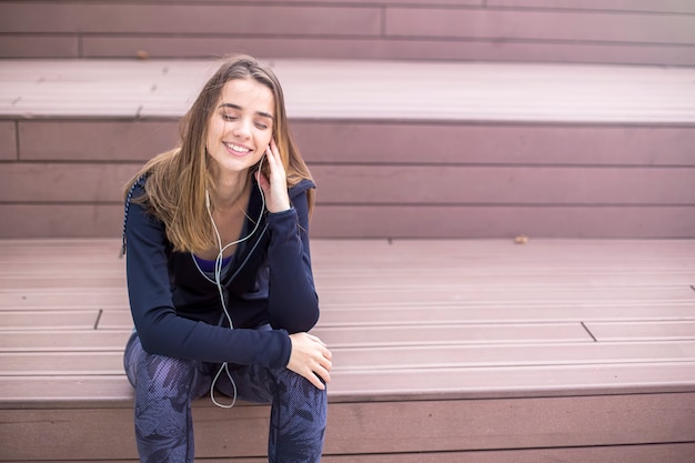 Young sporty woman resting and listen music on mobile phone after training outdoor in urban enviroment