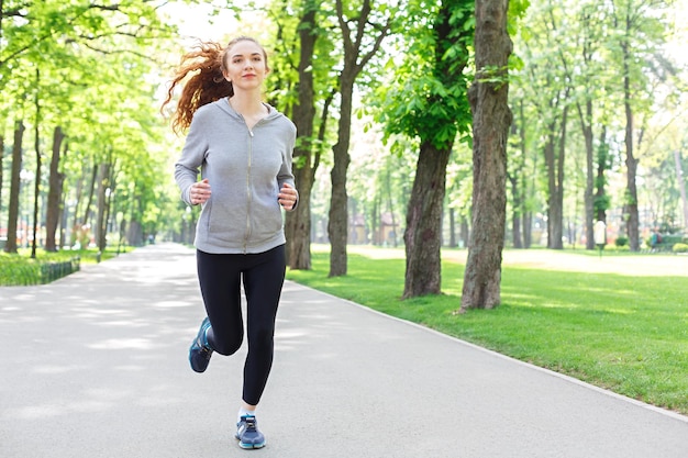 Young sporty woman running in green park during morning workout, copy space