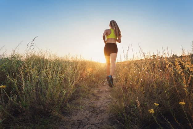 Young sporty woman running on a rural road at sunset