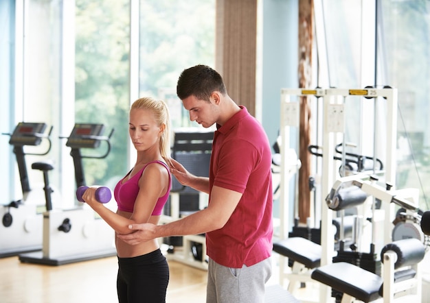 young sporty woman with trainer exercise weights lifting in fitness gym