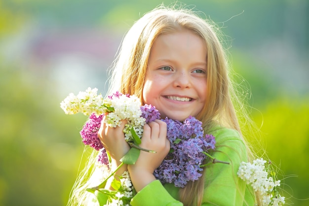 Young spring girl in spring garden. Young lady feeling happy in nature. Facial portrait of funny teenager girl. Girl with bouquet of lilac.