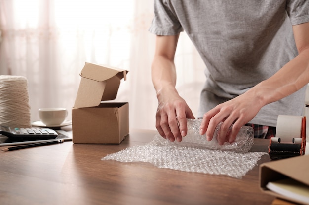 Young startup business owner packing products in shockproof plastic for sent to customer