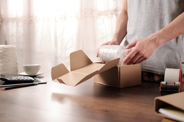 Young startup business owner packing products in shockproof plastic for sent to customer