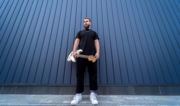 Young street musician playing guitar near the big blue wall