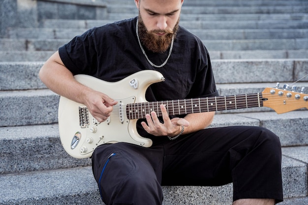 Young street musician playing guitar sitting on granite steps