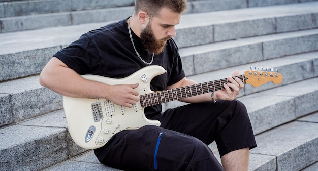 Young street musician playing guitar sitting on granite steps