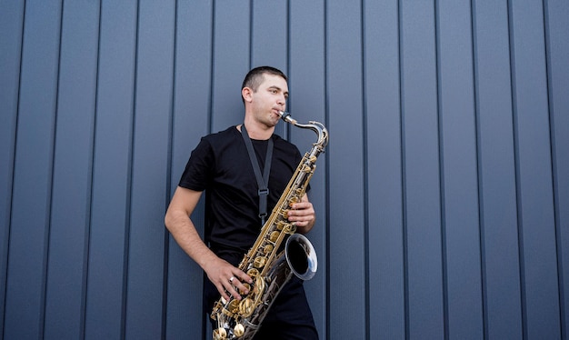 Young street musician playing saxophone near the big blue wall