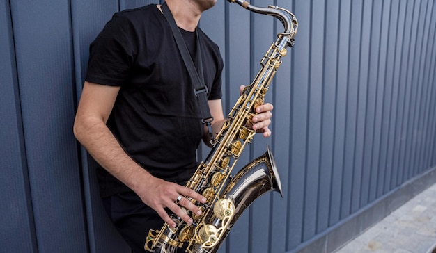 Young street musician playing saxophone near the big blue wall