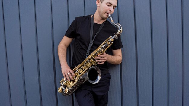 Young street musician playing saxophone near the big blue wall