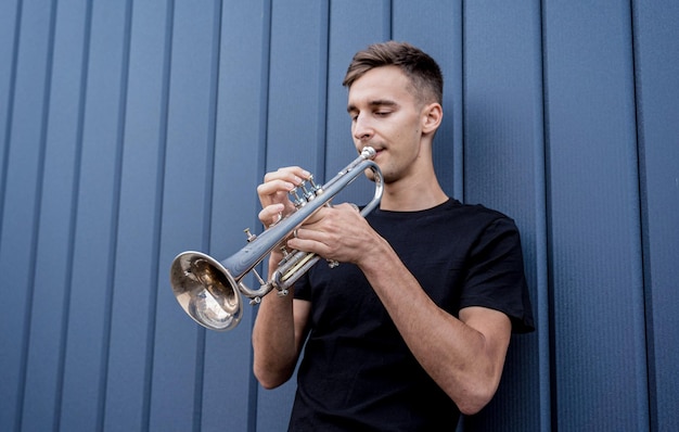 Young street musician playing the trumpet near the big blue wall