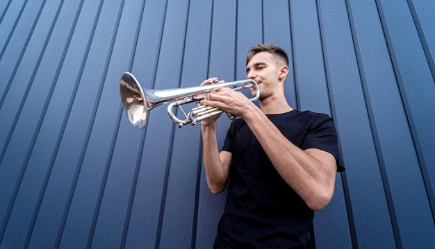 Young street musician playing the trumpet near the big blue wall