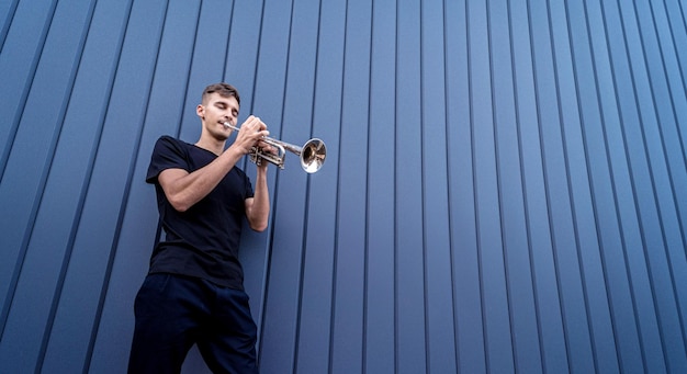 Young street musician playing the trumpet near the big blue wall