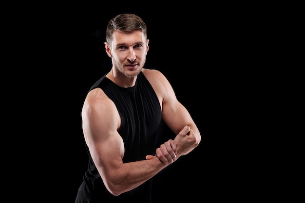 Young strong athlete in black sportswear keeping one hand on wrist of the other while showing his strength