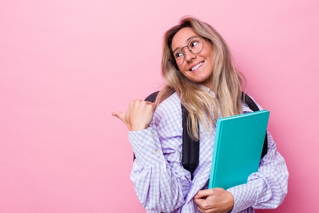 Young student australian woman isolated on pink background points with thumb finger away, laughing and carefree.