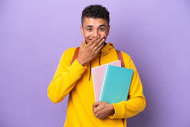 Young student Brazilian man isolated on purple background happy and smiling covering mouth with hand