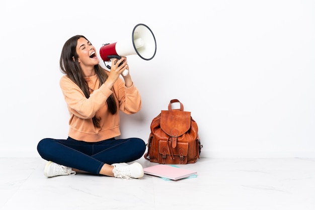 Young student brazilian woman sitting on the floor shouting through a megaphone