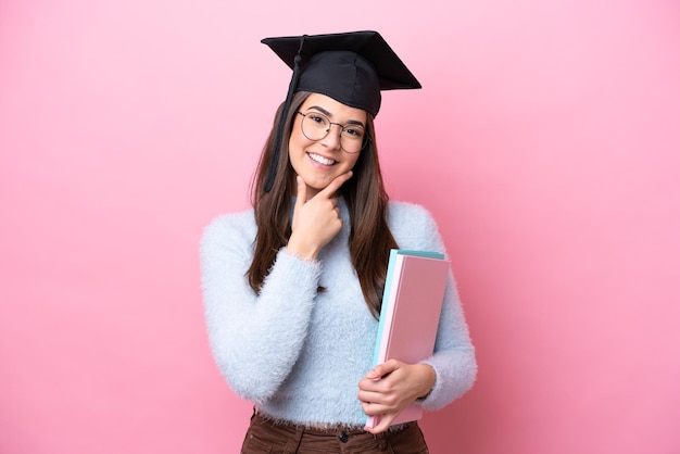 Young student Brazilian woman wearing graduated hat isolated on pink background happy and smiling