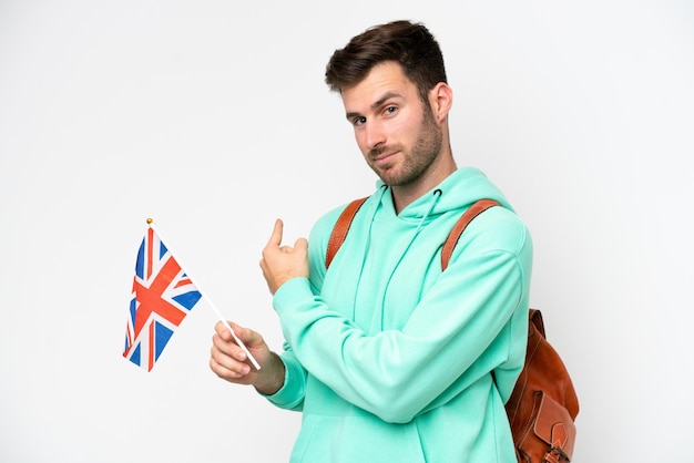 Young student caucasian man holding an United Kingdom flag isolated on white background pointing back