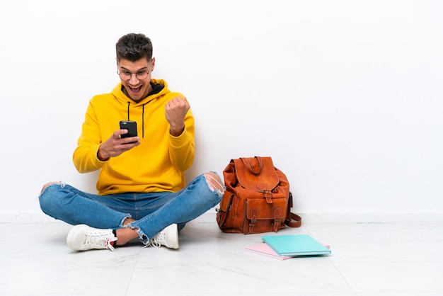 Young student caucasian man sitting one the floor isolated on white background surprised and sending a message