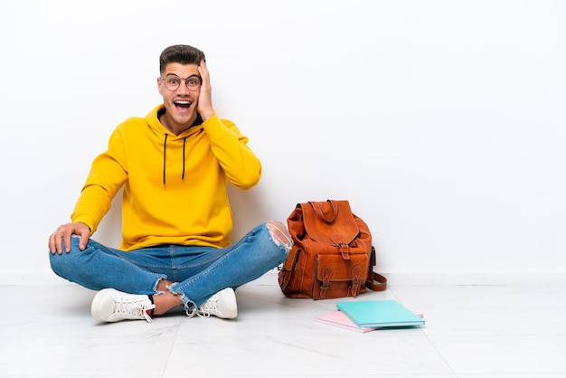 Young student caucasian man sitting one the floor isolated on white background with surprise and shocked facial expression