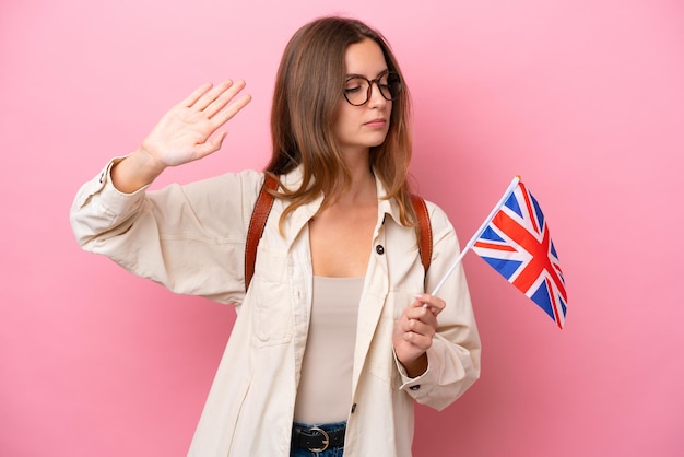 Young student caucasian woman holding an United Kingdom flag isolated on pink background making stop gesture and disappointed